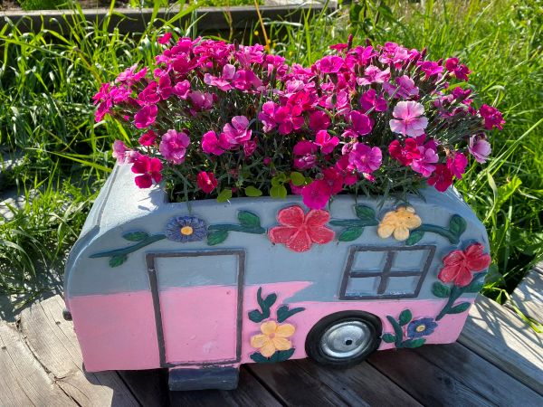 Blommor planterade i en kruka som ser ut som en husvagn. På Strömgården 1884 ställplatser.